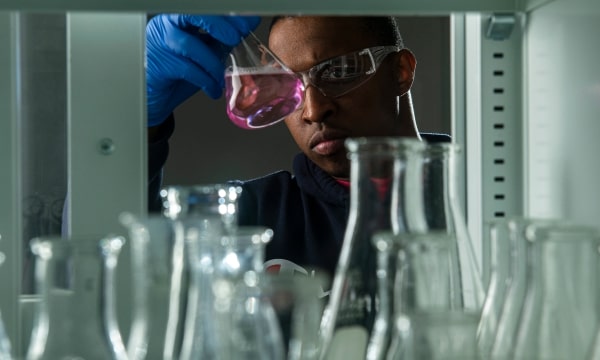 Lab student studying a beaker filled with pink liquid